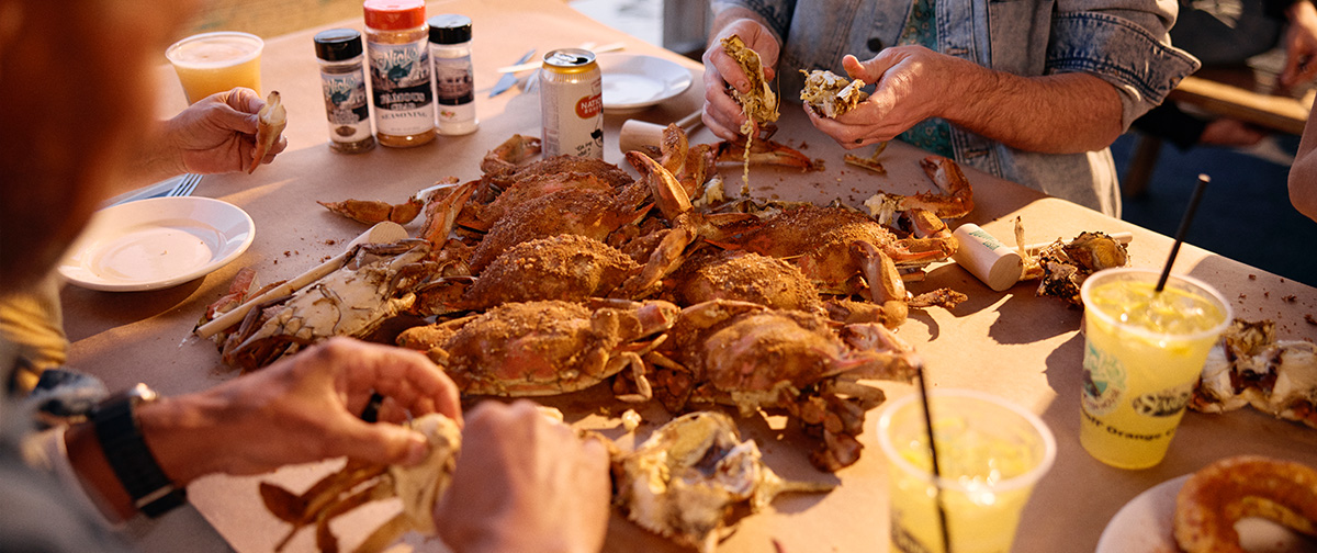 A group of people gather around a table covered with steamed crabs, cracking shells and eating together outdoors.