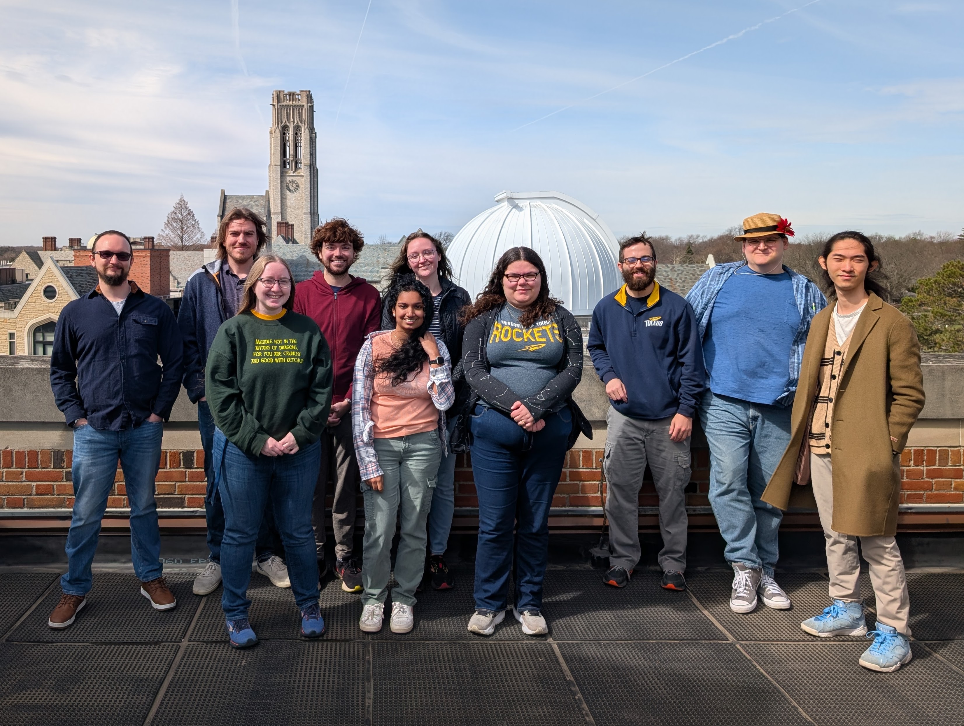 UT graduate students who have participated in outreach over the last calendar year taking a group photo with UT’s Ritter observatory and University Hall’s bell tower in the background. There are ten students in the photo. However, a total of sixteen graduate students have participated in outreach this year.